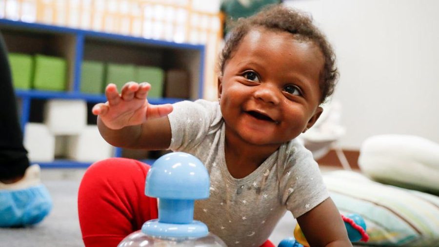A smiling infant reaching for a toy