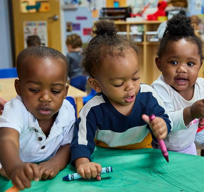 Toddlers drawing with crayons at a table